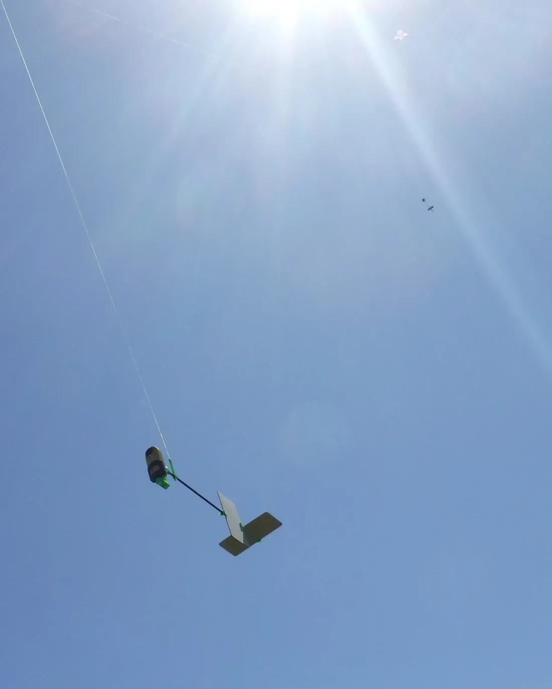 An Aeropod Profiler hanging from a kite line against a bright sky